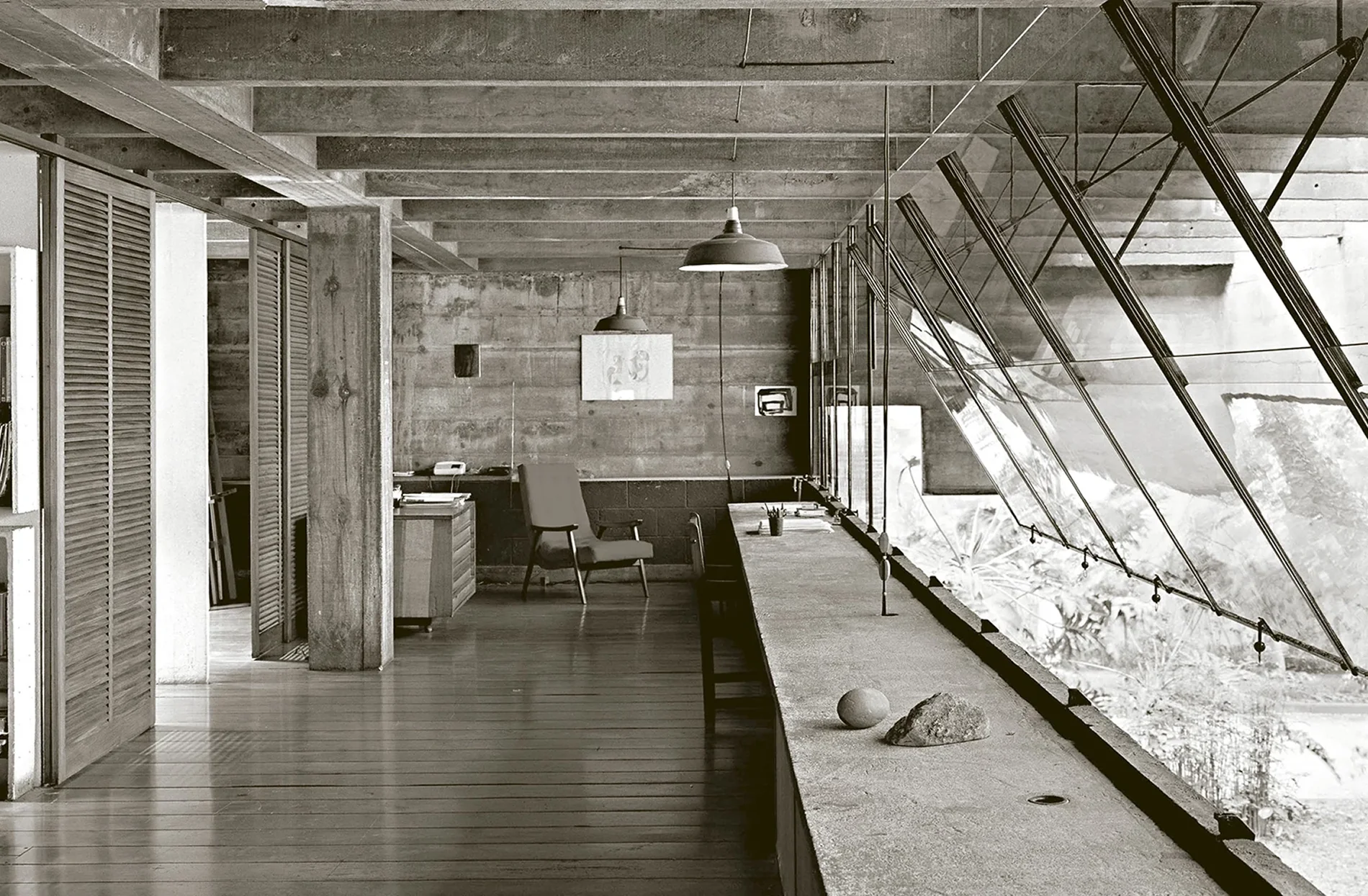 Brutalist office with a long raw concrete work surface, wooden floor and slanted glass wall
