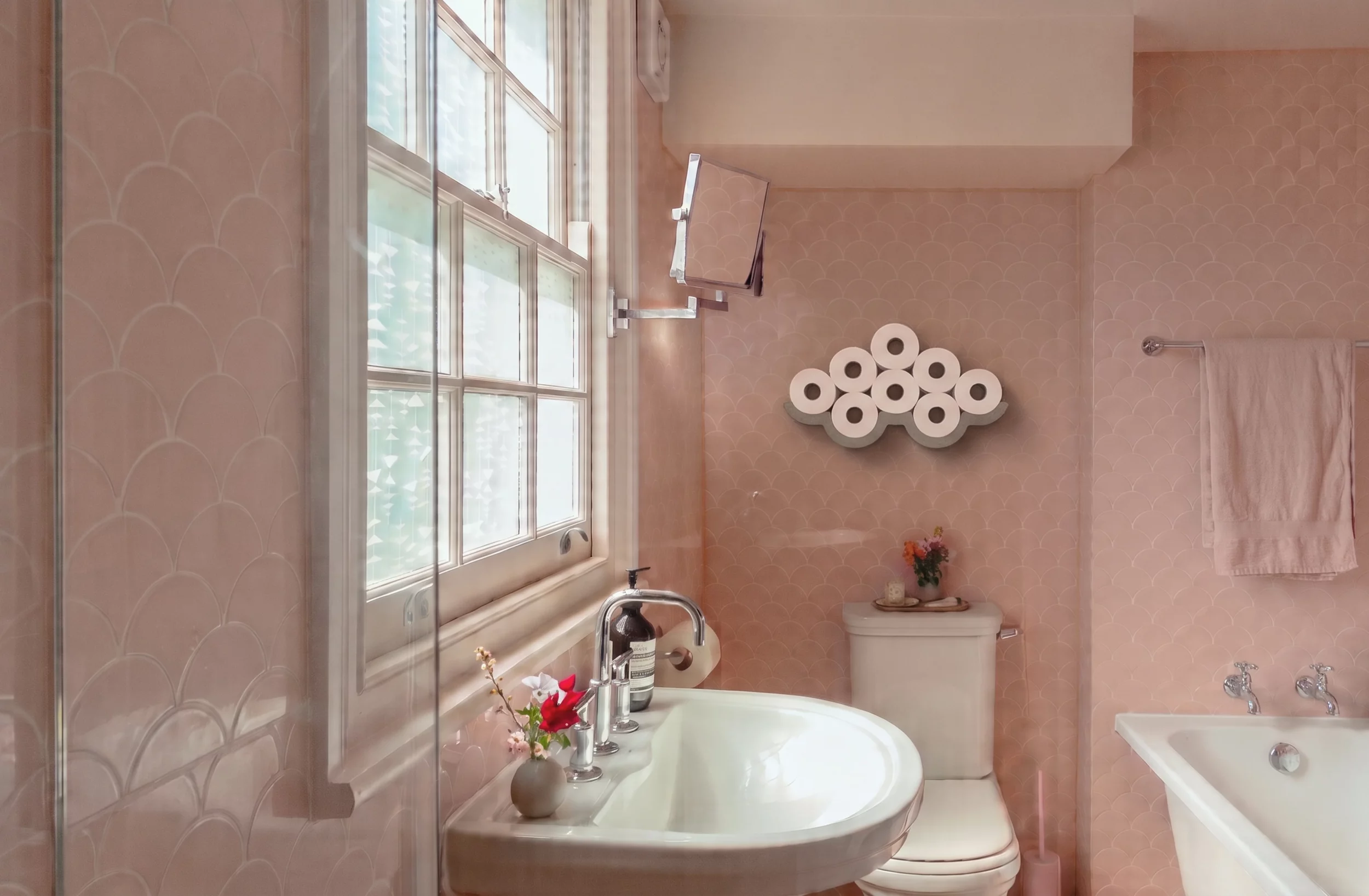 Concrete Cloud toilet paper holder filled with rolls, in a bathroom with pink tiles.