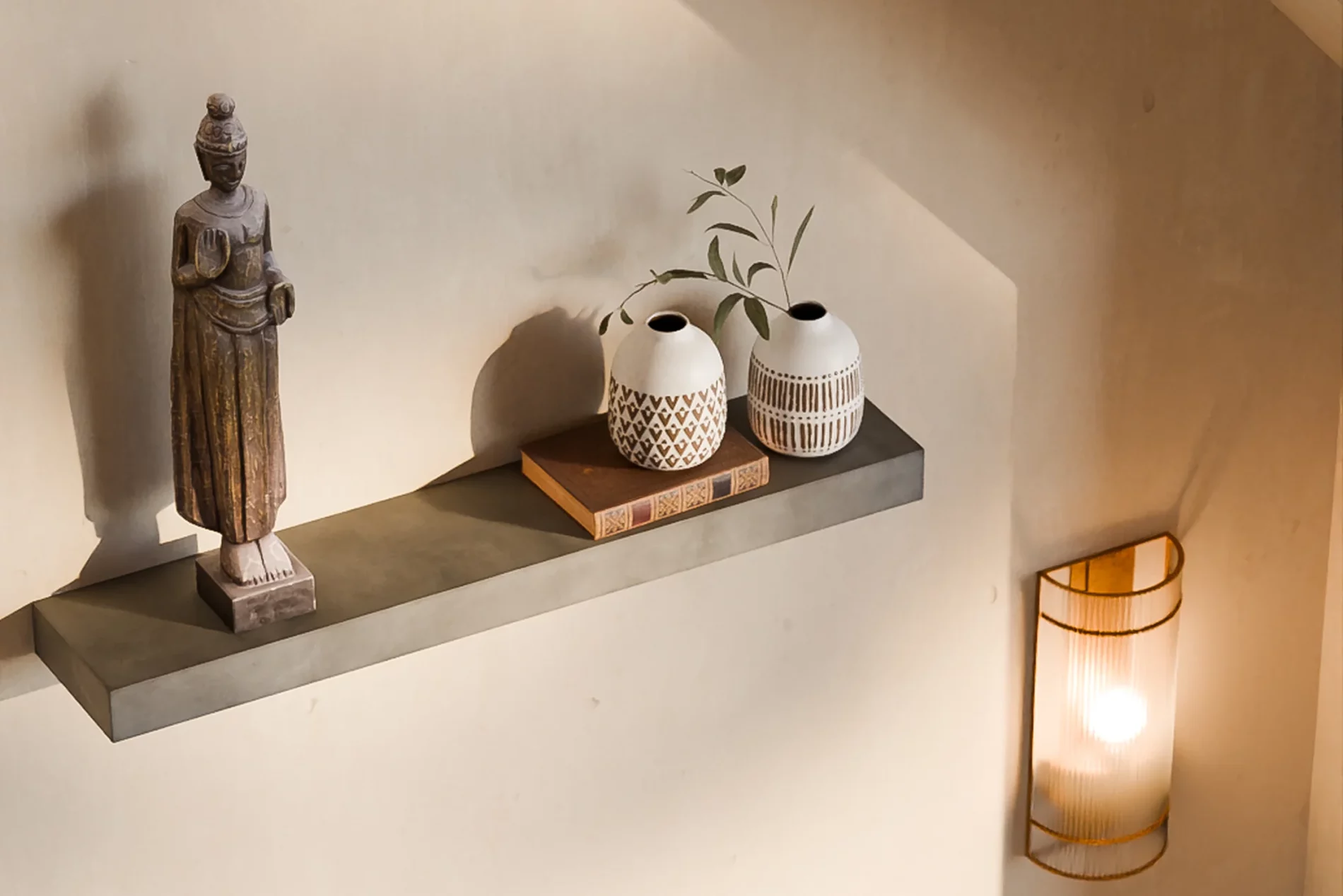 Concrete Sliced shelf with a wooden statue, a book and two ceramic vases.